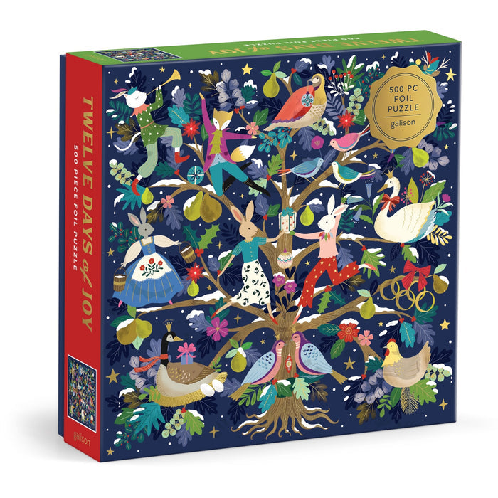 The Flora Waycott 12 Days of Joy 500 Piece Foil Puzzle features a festive illustrated tree with animals, birds, and people celebrating the Twelve Days of Christmas on a dark blue background.