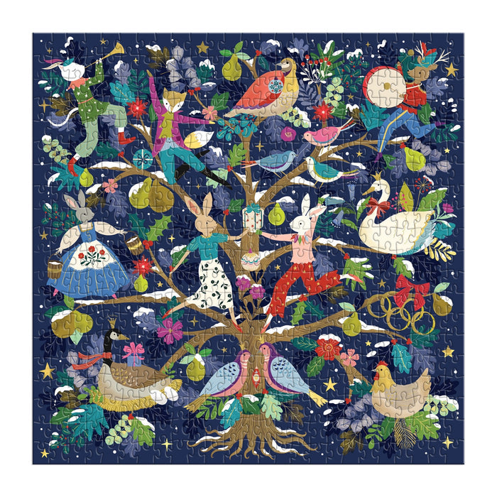 The Flora Waycott 12 Days of Joy 500 Piece Foil Puzzle features a whimsical tree with animals, birds, and human-animal figures among pears, flowers, leaves, and stars on a dark blue background.