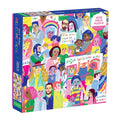The All Are Welcome Here! 1000 Piece Family Puzzle by Sarah Walsh features diverse illustrated people holding positive signs like “BE KIND” and “WELCOME HERE.” The box reads “ALL ARE WELCOME HERE” and “CELEBRATE DIVERSITY.”.