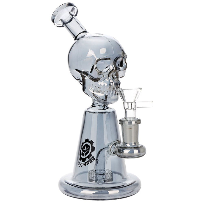A clear glass skull water pipe with a metallic silver base and a glass bowl attachment, featuring a black logo on the neck, set against a plain white background.