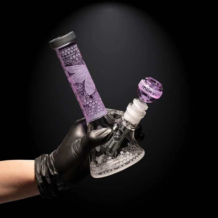 Glass water pipe with purple accents held by a gloved hand against a black background