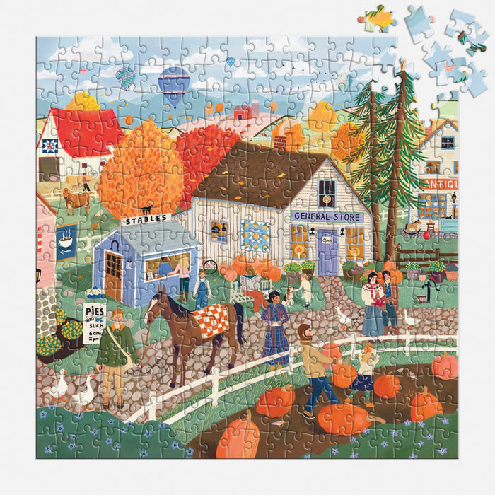 The Autumn Square 300 Piece Puzzle by Elisabeth Dorrian features a vibrant fall village with people, pumpkins, animals, and charming shops among autumn trees. A few pieces are missing in the top right section of this lively scene.