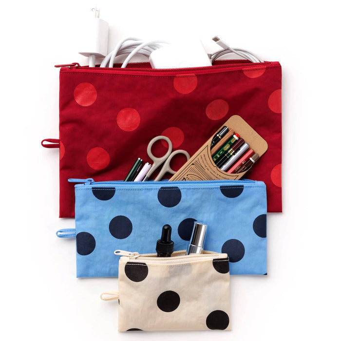3 flat zip pouches with polka dots, top is red with charger cords, middle is blue with pencils, pens, and scissors and the bottom is cream with black dots with makeup, all on a white background.