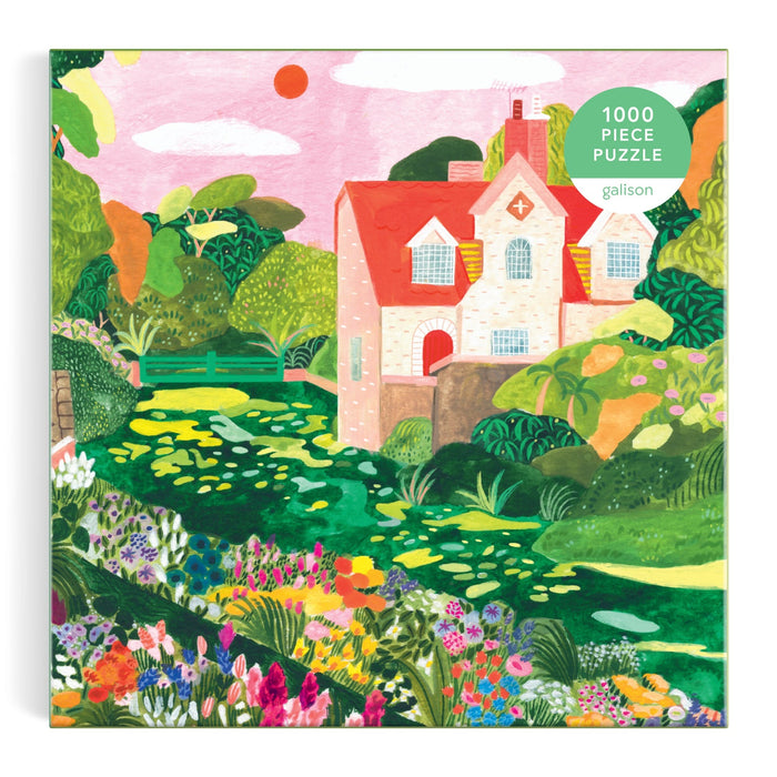 A colorful illustration of a house with a red roof, gardens, trees, and flowers under a pink sky with a red sun appears on the box of the Blooming Meadow 1000 Piece Puzzle by Flore Cousseran.