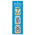 The Christine De Carvalho Blooming Terrariums Magnetic Bookmarks set features three bookmarks with illustrated designs: a bird among flowers, a bouquet of flowers, and two butterflies with flowers in a blue package.
