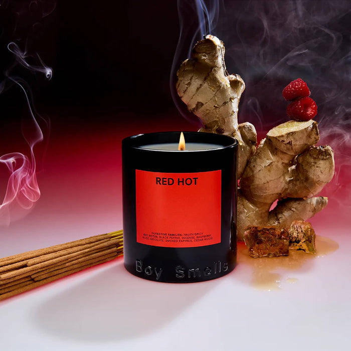 Boy Smells Red Hot scented 9 ounce Classics candle in black glass vessel with dark red label, with ginger, incense and raspberries in the background.