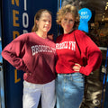 Two people wearing 'Brooklyn' sweatshirts standing in front of a blue wall with text.