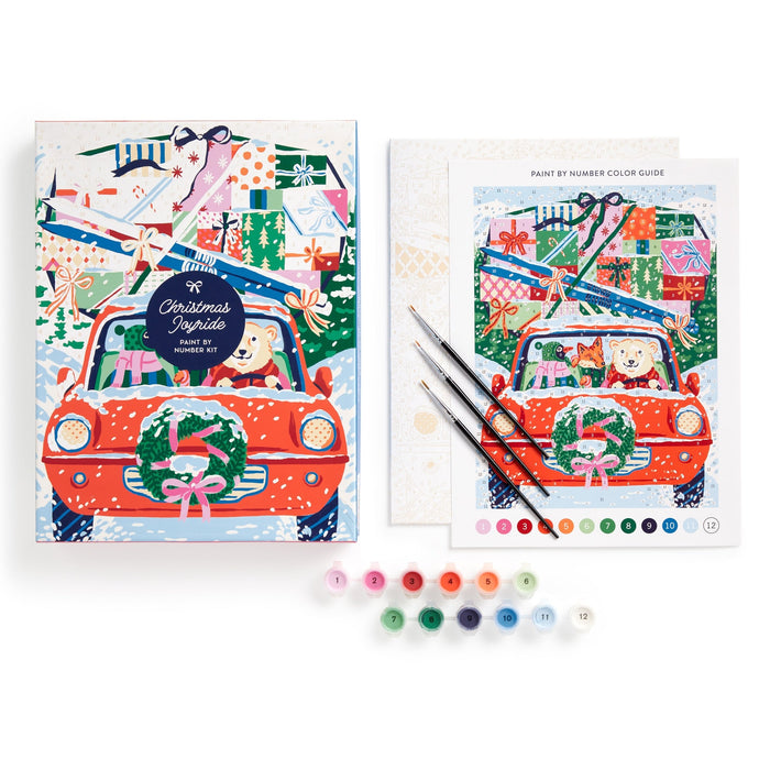 The Emily Taylor Christmas Joyride 9 x 12" Paint by Number Kit features a car with a wreath, two dogs, and gifts. Includes canvas, paint guide, brushes, and numbered paint pots in assorted colors.