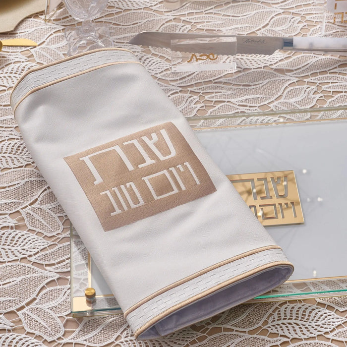 Classic 2.0 Challah Cover in cream and tan leather with gold-tone hardware detail, displayed on decorative fabric.