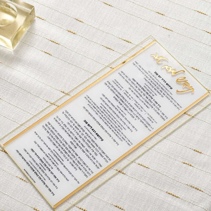 Classic Kiddush Yom Tov gold-trimmed lucite card with Hebrew text on white background, displayed on striped surface with glass nearby.