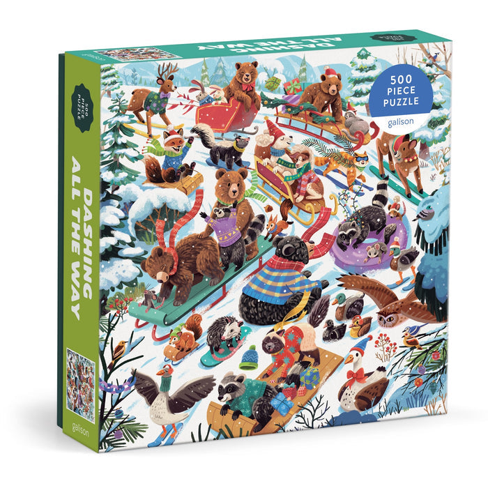 The Lucia Baertl "Dashing All the Way" 500 Piece Puzzle features winter animals—bears, raccoons, foxes, and more—sledding on a snowy hill in a festive scene with trees and snow-covered ground.