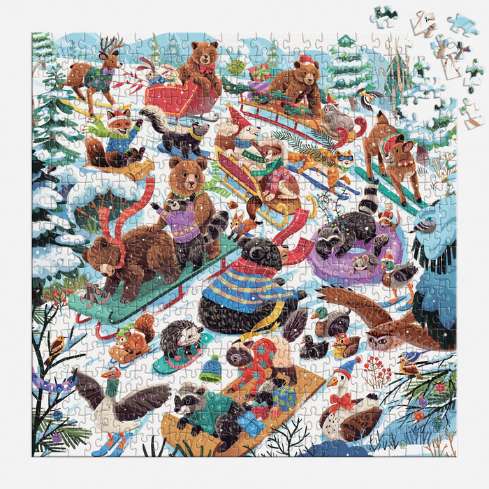 The Dashing All the Way 500 Piece Puzzle by Lucia Baertl depicts animals like bears, deer, raccoons, and beavers sledding on a snowy hillside among trees and birds. A few pieces are missing in the top right corner.