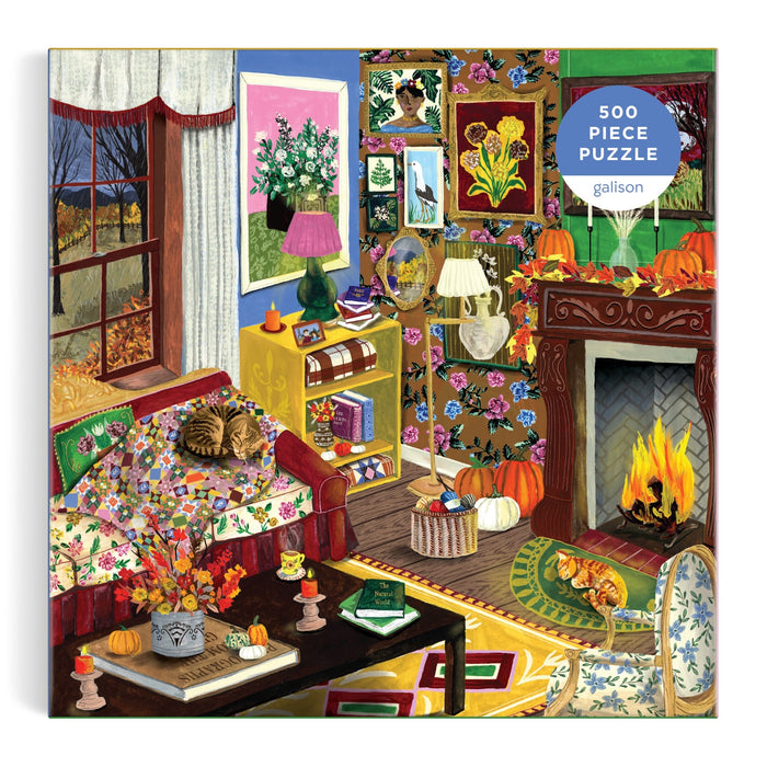 Enjoy a cozy living room scene with a cat lounging on a floral couch, a fireplace aglow with fire, autumn decorations, books, and art adorning the walls—plus a window framing a beautiful fall landscape. This charming image is featured on Abby Jacobs' Fall is in the Air 500 Piece Puzzle—a perfect rainy day activity, beautifully packaged in an eye-catching box.