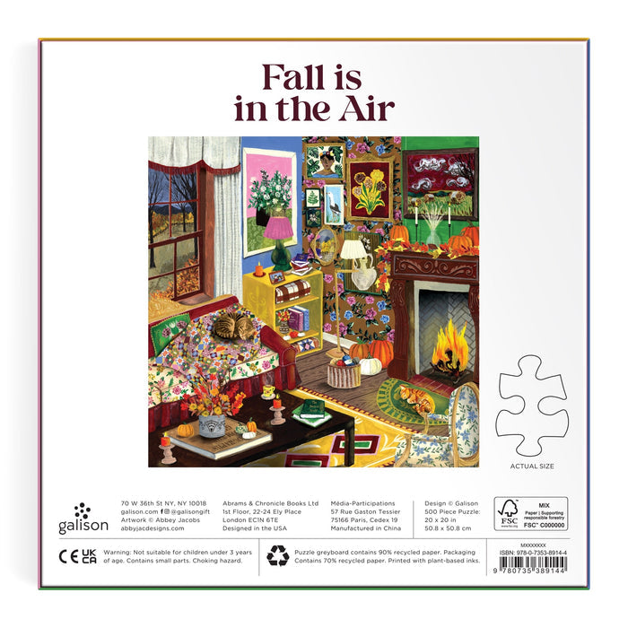 Discover the "Fall is in the Air 500 Piece Puzzle" by Abby Jacobs—a cozy autumn living room scene complete with charming fall decor, a glowing fireplace, pumpkins, books, and a cat nestled on a chair. Colorful autumn leaves can be seen through the window, enhancing the warm and inviting atmosphere. Ideal for anyone seeking a delightful rainy day activity or an autumn-themed illustrated puzzle to enjoy at home.