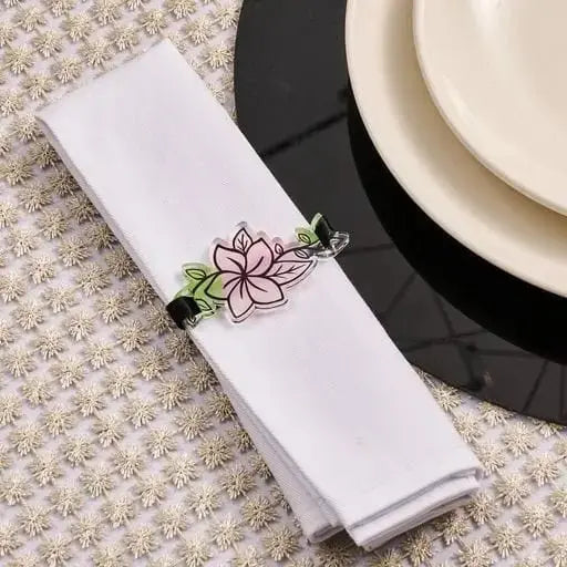 Floral napkin wrap with pink flower design and green leaf detail on white linen napkin, displayed with place setting.