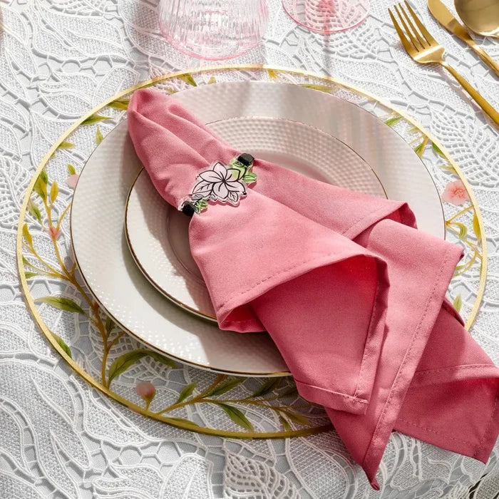 Pink floral napkin wrap with gold napkin ring holder displayed on white plate with formal table setting