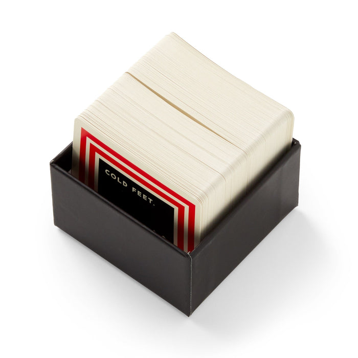 Brass Monkey’s Frivolous Holiday Trivia is a black box set of playing cards, bordered in red, white, and black—ideal for party games. The top card displays the phrase “COLD FEET.”.