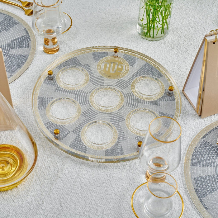 Geometric Seder plate with clear lucite construction and gold accents, displayed on a table setting with wine glasses and place settings for Passover.