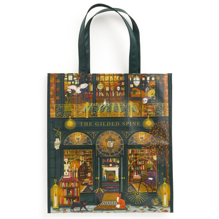 The Gilded Spine Reusable Shopping Bag by Sally Wilson features a cozy, two-story bookstore with books, animals, autumn leaves, and warm yellow lights. A person and cat read outside, adding to its charming illustrated design.
