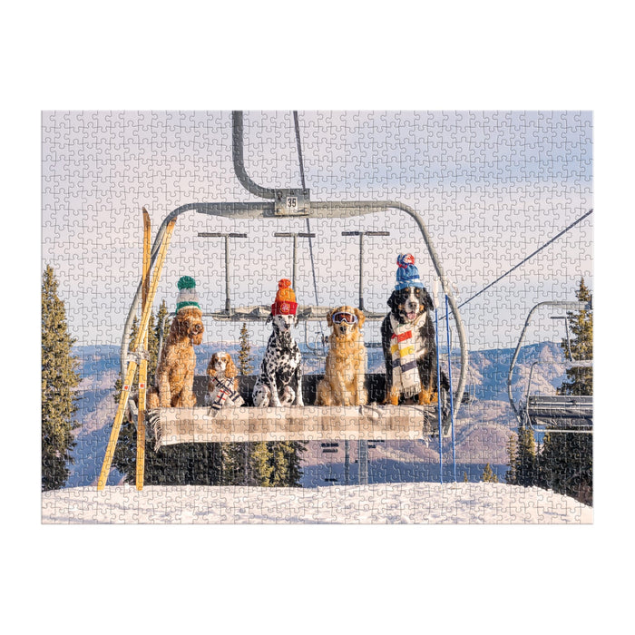 Five dogs in winter hats and scarves sit on a ski lift above snowy mountains and pine trees, evoking Aspen’s charm in Gray Malin’s fine art style, featured on the Gray Malin Aspen 1000 Piece Book Box Puzzle by Gray Malin.