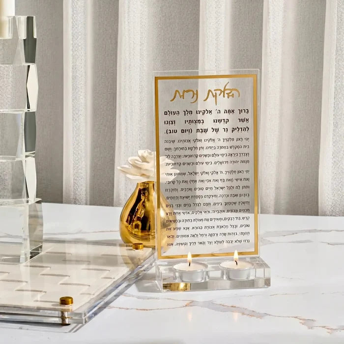Gold Hadlokas Neiros tea light holder with prayer card displayed on white marble surface, featuring elegant candle-lighting design for Shabbat.