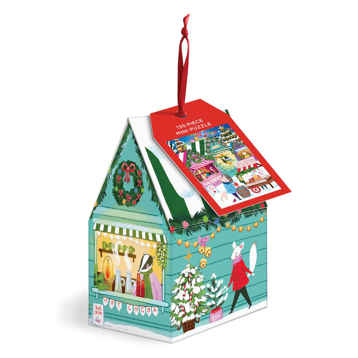 The Joanna Clay Holiday Market 130 Piece Puzzle Ornament is a house-shaped box with festive holiday designs and animals decorating a Christmas tree. It features a red hanging ribbon and a tag with the finished puzzle image.