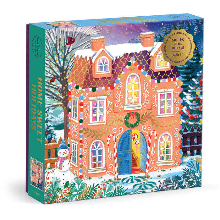 The Joanna Clay Home Sweet Holidays 500 Piece Foil Puzzle features a festive gingerbread-style house with a wreath, snowy trees, and a snowman—perfect for holiday fun.