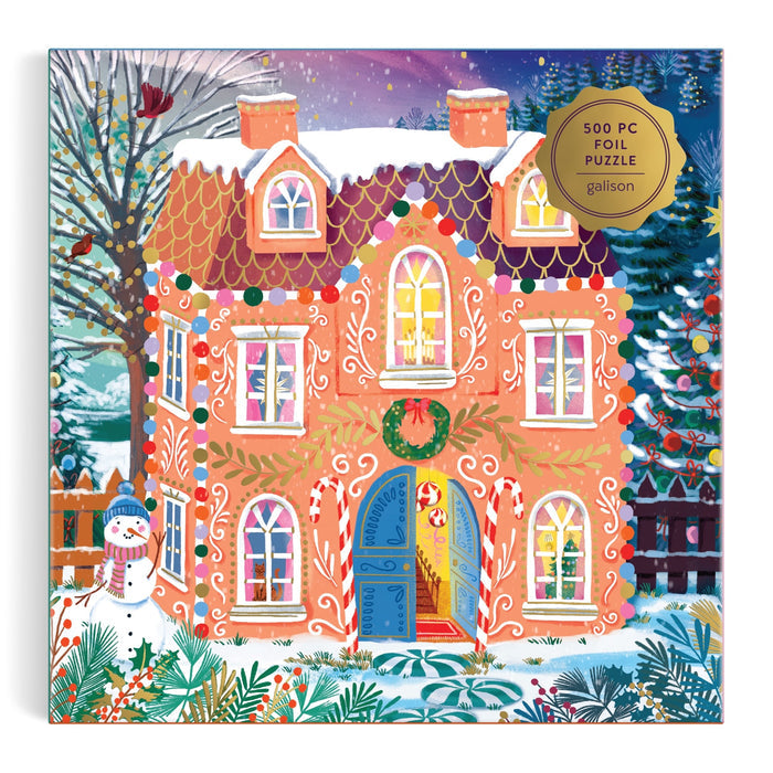 A colorful illustration of a gingerbread-style house decorated for winter, with a snowman in the yard, features on the "Home Sweet Holidays 500 Piece Foil Puzzle" by Joanna Clay.