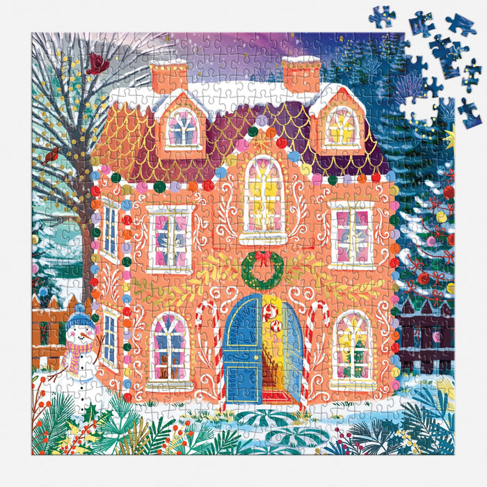 The Joanna Clay "Home Sweet Holidays" 500 Piece Foil Puzzle features a vibrant gingerbread house with festive decor and snowy surroundings. Some blue pieces remain unplaced in the top right corner.