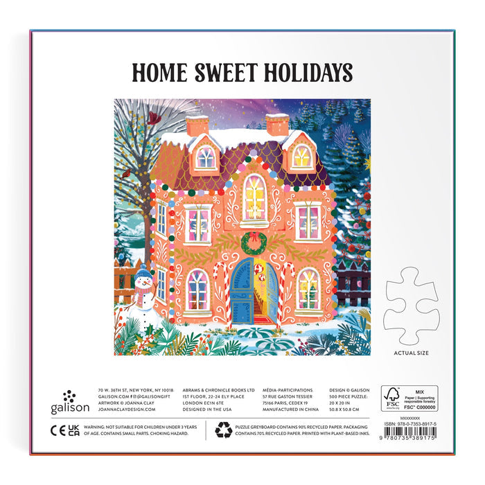 Festive illustration of a gingerbread-style house with lights, wreaths, snowy trees, and a smiling snowman. “Home Sweet Holidays” text above. Home Sweet Holidays 500 Piece Foil Puzzle by Joanna Clay.