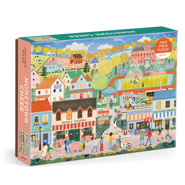 Hometown Cheer 1000 Piece Puzzle by Elisabeth Dorrian features a vibrant small town scene with shops, a pizzeria, market stalls, people strolling, trees, and houses.