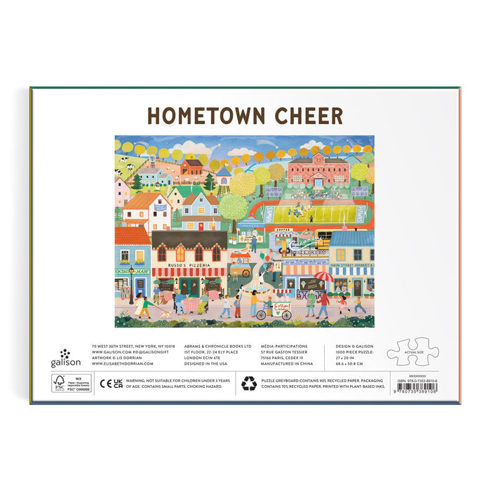 Box back for the Elisabeth Dorrian Hometown Cheer 1000 Piece Puzzle, featuring a vibrant small-town scene with people, houses, shops, trees, blue sky, clouds, and balloons.