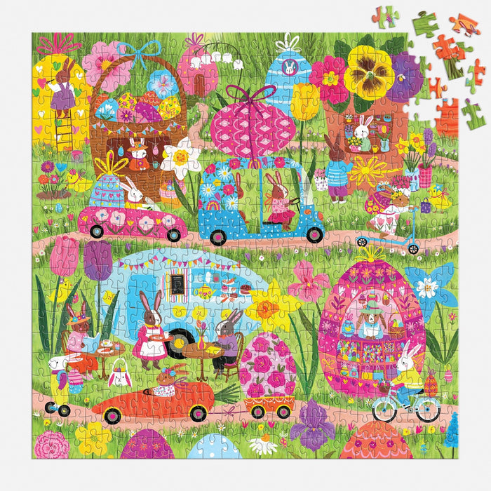 The Hoppin' Around 500 Piece Family Puzzle by Jenny Miriam features a whimsical bunny village with flower-shaped houses, cars, and bunnies among vibrant blooms—some pieces are missing in the top right corner.