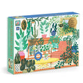The Houseplant Haven 1000 Piece Foil Puzzle by Faye Guanipa features a vibrant illustrated living room with potted plants, a striped orange sofa, and decorative accents on the colorful box.