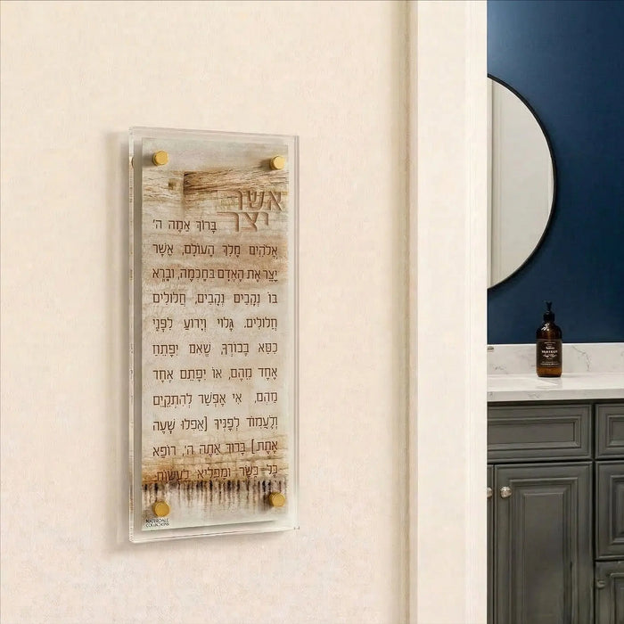 Taupe Kosel Asher Yatzar prayer art with Hebrew text and Jerusalem skyline design in wooden frame on cream wall.