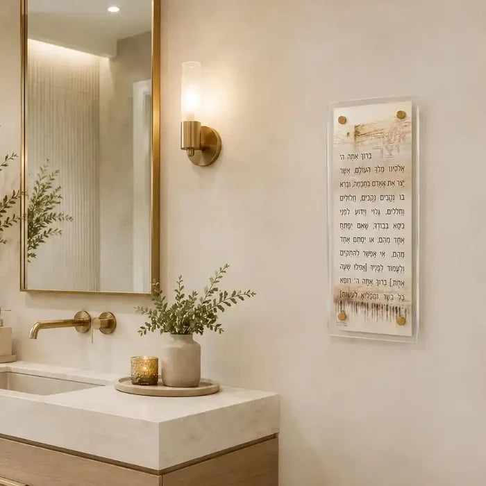 Taupe Kosel Asher Yatzar prayer art displayed above a bathroom sink with brass fixtures and greenery.