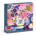 The Joy Laforme Art of the Table 500 Foil Piece Puzzle features a colorful floral tea table scene with flowers, fruit, butter, and bread against a pink background. Brand: Joy Laforme.