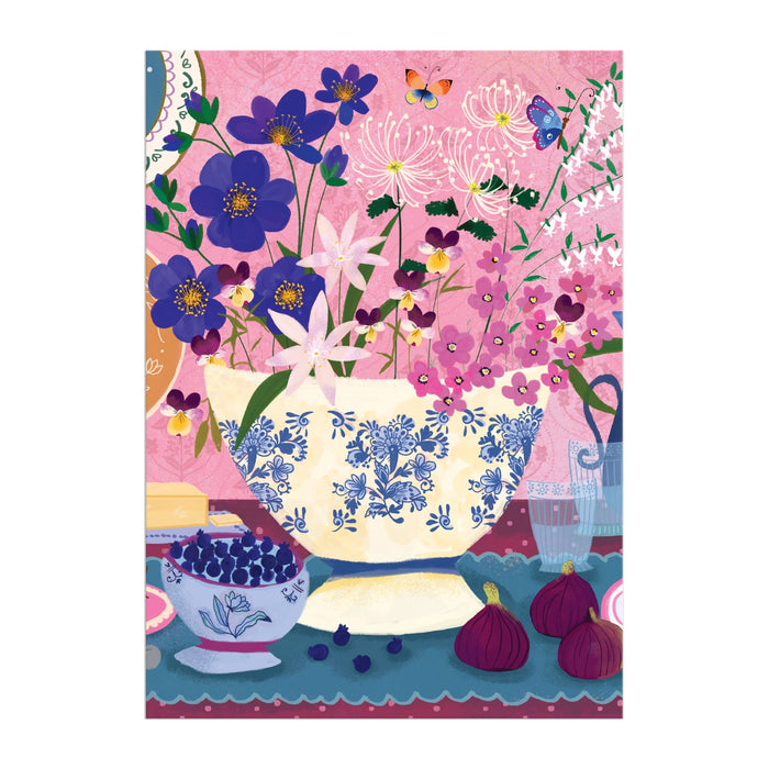 The Joy Laforme Art of the Table Greeting Card Puzzle by Joy Laforme features a decorative vase with colorful flowers, figs, blueberries, and a butterfly on a patterned table against a pink floral background.