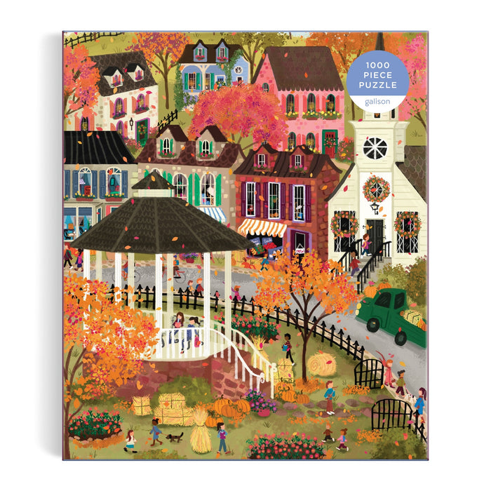 The Joy Laforme Falls Hollow 1000 Piece Puzzle shows a lively autumn village with colorful houses, people, children at play, orange trees, a white gazebo, hay bales, and pumpkins in the foreground. Brand: Joy Laforme.