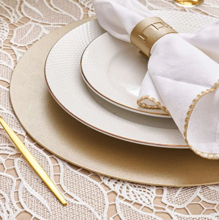 Waterdale leather round chargers in gold with white napkin and place settings arranged on neutral tablecloth for formal dining.