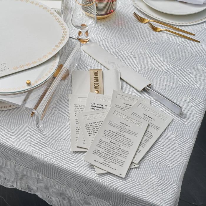 White leather Shabbos pouch displayed on white tablecloth with place setting, showing practical hostess gift for holiday entertaining.