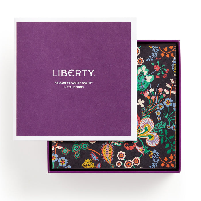 A partly open purple box lid labeled Liberty Origami Treasure Box Kit by Liberty of London Ltd reveals floral and bird origami folds in colorful Liberty patterns inside the kit.