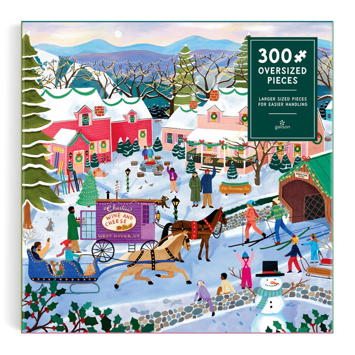 The Little Winter Town 300 Piece Puzzle by Elisabeth Dorrian features a snowy village scene with people ice skating, riding a horse-drawn sleigh, shopping, and enjoying winter fun. Colorful houses, snow-covered trees, and mountains complete the landscape.