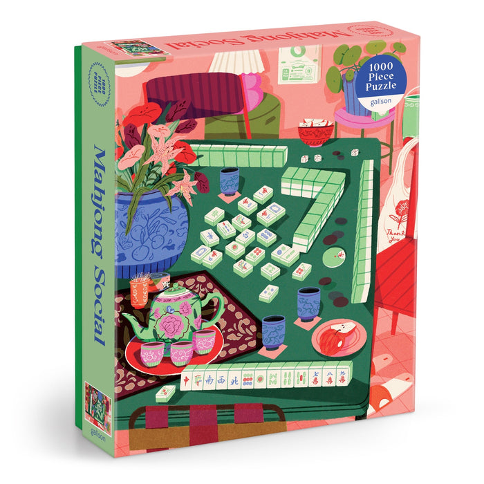 The Mahjong Social 1000 Piece Puzzle by Paige Jung showcases a vibrant illustration of a Mahjong game table with tiles, tea, snacks, flowers, and cozy decor in pink, green, and red hues.