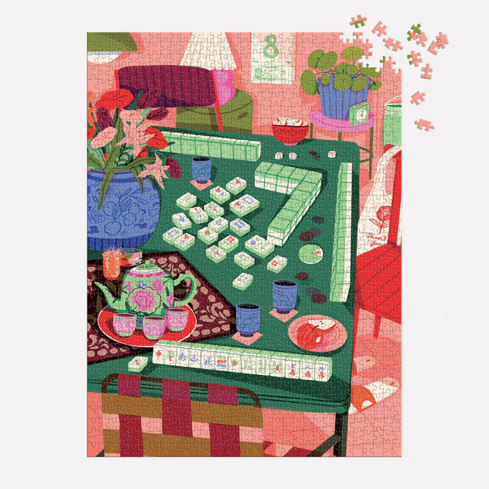 The Mahjong Social 1000 Piece Puzzle by Paige Jung features a cozy room scene with a Mahjong game on a green table, surrounded by teacups, flowers, and colorful furniture; some pieces remain to be placed.