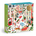 The Sabina Fenn Merriest Village 1000 Piece Foil Puzzle showcases a vibrant, snowy village street at Christmas, with people, cars, a sleigh, decorated trees, and festive garlands in a cheerful winter scene.