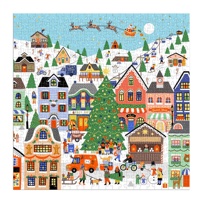 The Merryville 500 Piece Foil Puzzle by Holly Maguire features a winter village scene with colorful houses, a decorated Christmas tree, festive activities, snow-covered rooftops, a market, and Santa’s sleigh flying across a blue sky.