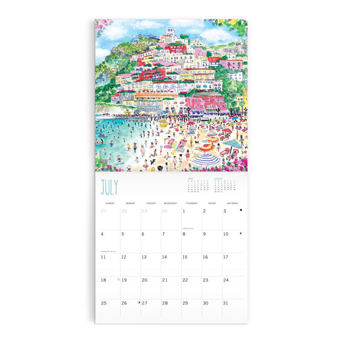 The Michael Storrings 12 x 12 Wall Calendar 2027 features a July page with a vibrant seaside town illustration—hillside buildings, busy beach, umbrellas, and blue water—by Michael Storrings. The calendar grid appears below the artwork.
