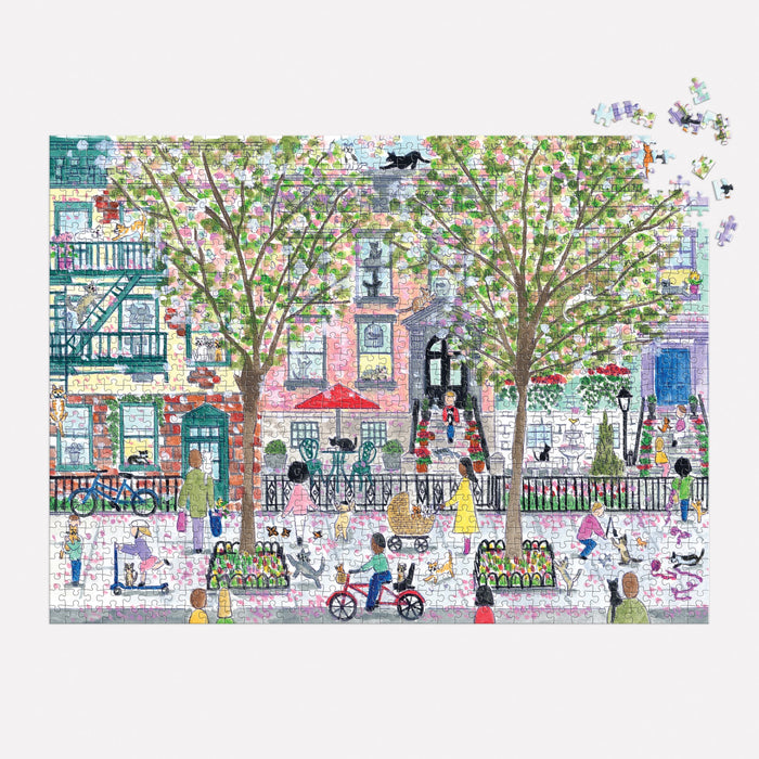 The Michael Storrings Cats in the City 1000 Piece Puzzle by Michael Storrings features a vibrant city street with people and blossoming trees, plus charming cafes and apartments—ideal for puzzle fans and lovers of lively city scenes.