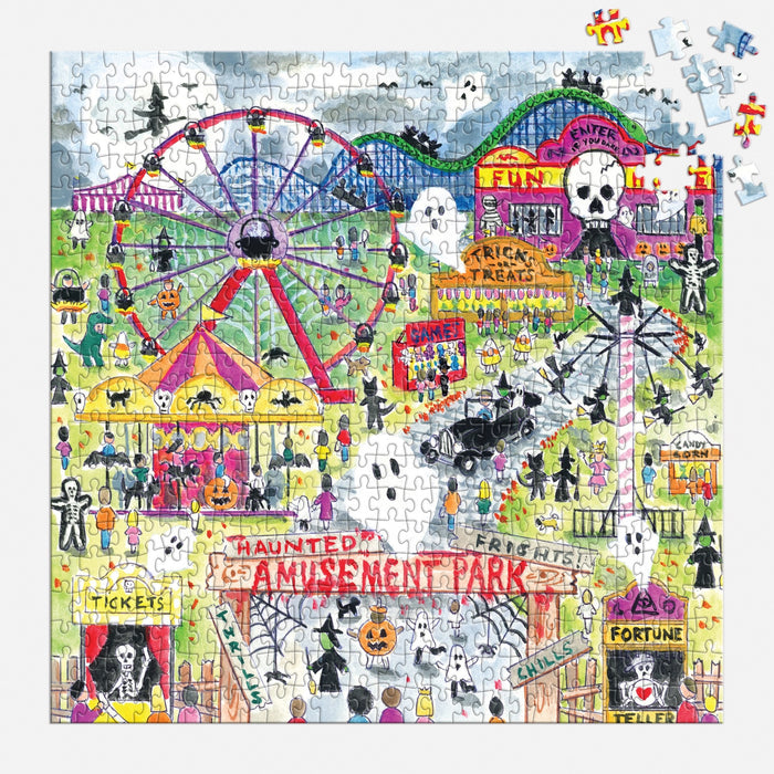 The Michael Storrings Haunted Amusement Park 500 Piece Puzzle by Michael Storrings shows a lively haunted amusement park with people in costumes, skull decorations, spooky rides, and a few missing pieces in the corner.
